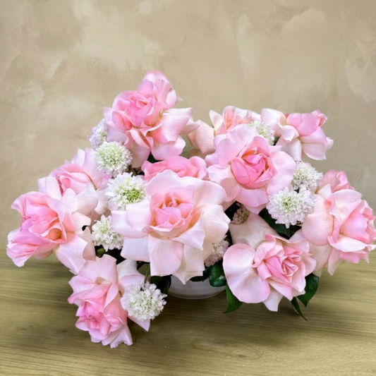 Decorative arrangement of pink and white flowers on a wooden surface with a beige background