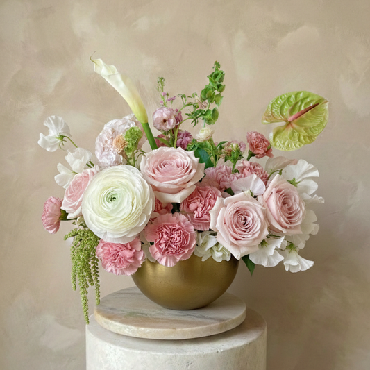 Floral arrangement in a gold vase on a white pedestal against a beige background