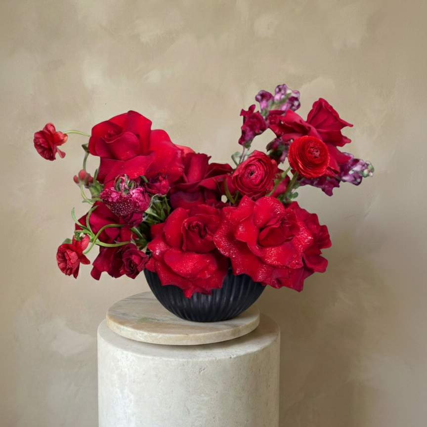 Bouquet of red flowers in a black vase on a white pedestal against a beige background